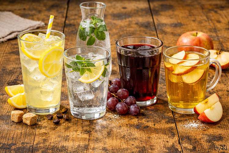 Alkoholfreie Getränke – Limonade, Wasser, Traubensaft und Apfelsaft<br />
Vier erfrischende Getränke stehen nebeneinander auf einem rustikalen Holztisch:</p>
<p>Limonade: Hellgelb und spritzig, mit Eiswürfeln und Zitronenscheiben im Glas. Der Duft ist frisch und leicht säuerlich, die Oberfläche glitzert im Licht.</p>
<p>Wasser: Kristallklar mit Minzblättern und Eiswürfeln, leicht beschlagenes Glas, das Kühle und Frische vermittelt.</p>
<p>Traubensaft: Tiefrot und samtig, mit frischen Trauben auf dem Tisch. Der Geruch ist süß und fruchtig, die Farbe intensiv und warm.</p>
<p>Apfelsaft: Goldgelb und klar, mit Apfelscheiben im Glas und daneben auf dem Tisch. Der Duft ist mild, fruchtig und erinnert an reife Äpfel.</p>
<p>Das Licht ist hell und natürlich, die Stimmung freundlich und sommerlich. Die Szene vermittelt Frische, Leichtigkeit und natürliche Vielfalt.